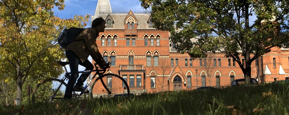 Student biking past Sage Hall