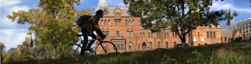 Student biking past Sage Hall