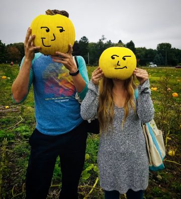 Students holding smiley face pumpkins in front of faces