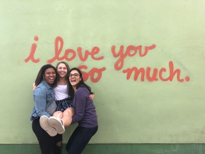 Three students against mural saying, "I love you so much"