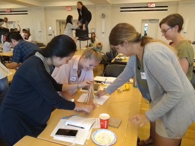 Students using dry spaghetti, marshmallows, and tape to form a tall structure.