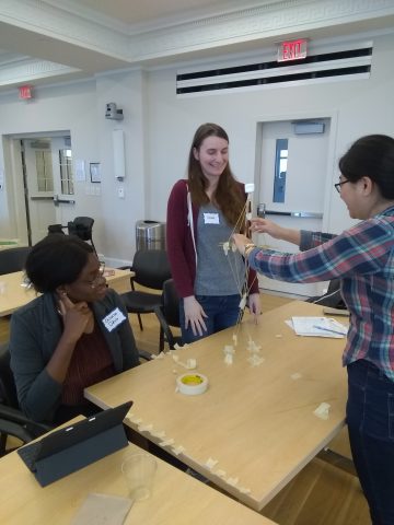 Students using dry spaghetti, marshmallows, and tape to form a tall structure.