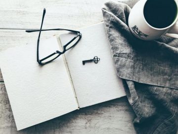 Glasses on blank notebook pages next to a cup of coffee