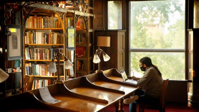 A student wearing a face mask and studying in the library