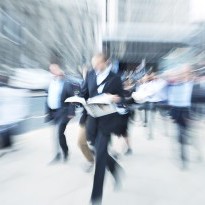 Blurred image of man holding a newspaper walking through a crowd