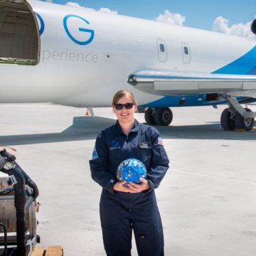 Laura Jones-Wilson holding a globe and standing in front of a plane