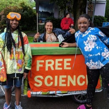 Three kids stand in front of a table with a banner reading, "Free Science"