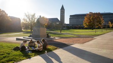 A group of students works together on the Arts Quad with McGraw Tower in the background