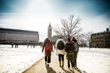 A ground of students in winter gear walk across the snowy quad toward McGraw Tower