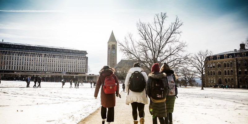 A group of students in winter gear walk across the snowy quad toward McGraw Tower