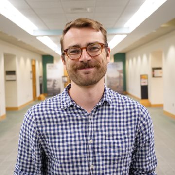 Bruno Shirley in a checked shirt and glasses in a hallway