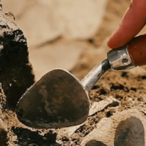 A person holds a small shovel above dirt