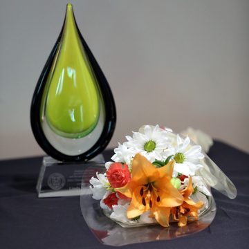 A green teardrop shaped award sits on a table next to a bouquet of flowers