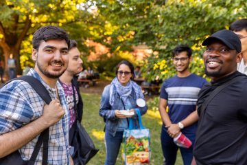 Incoming students stand in a circle, smiling at the camera, during the new student ice cream social