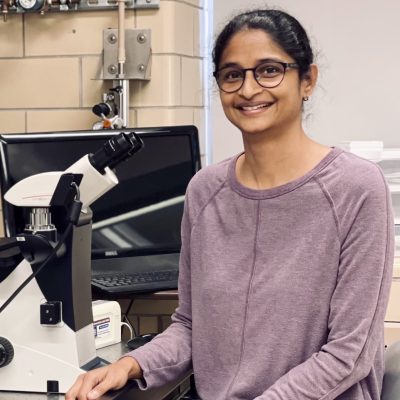 Prasanthi Koganti stands next to a microscope