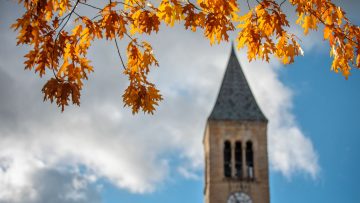 Fall leaves hang in front of McGraw Tower against the backdrop of a clouded blue sky