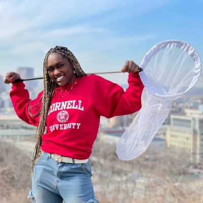 Sylvana Ross wears a Cornell sweatshirt and holds an insect-catching net over her shoulders