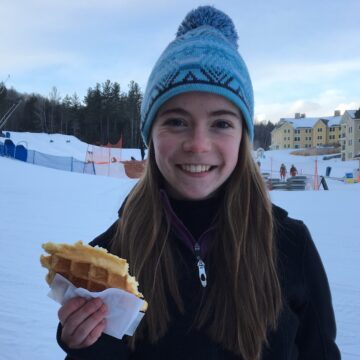 Lauren stands outside on a ski slope with a waffle