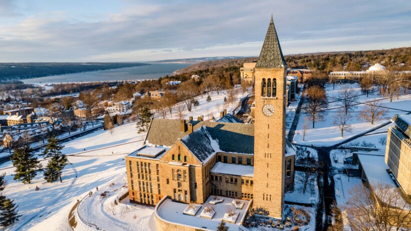 An aerial view of Cornell's Ithaca campus with McGraw Tower in the foreground and Cayuga Lake in the background after snowfall