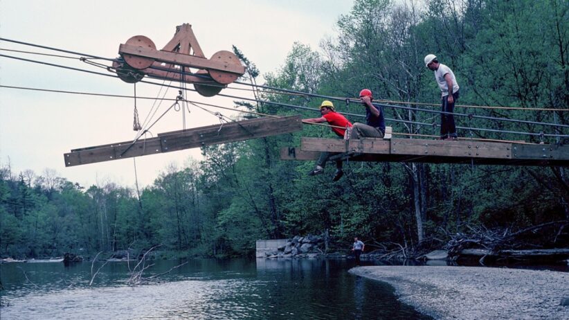 Students sit on part of a constructed bridge while constructing the rest