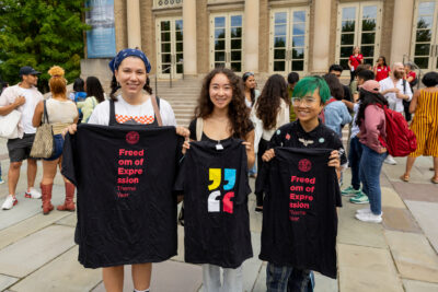 Three graduate students hold up freedom of expression theme year shirts at the 2023 Dean's Welcome