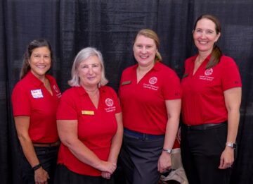 Four women in red Graduate School logo shirts standing at an event booth