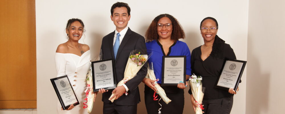 four people standing together holding flowers and award plaques