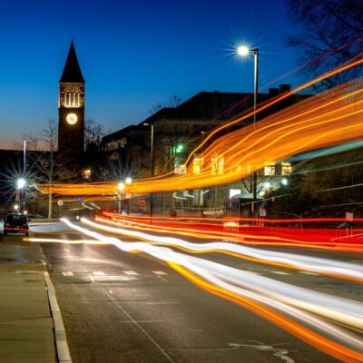 McGraw Tower is seen at night as cars and busses pass by on Tower Road in a long exposure photograph.