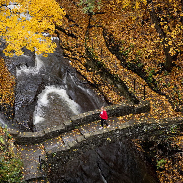 An aerial view of a student crossing a stone bridge on the Cornell campus