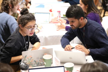 two individuals looking at their laptop screens and discussing the content