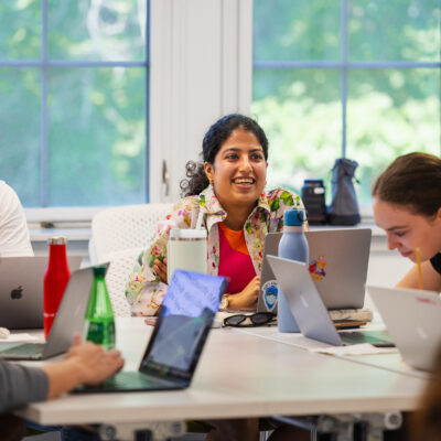 Students sit around a table with laptops in front of them