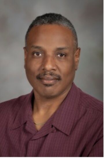 Formal photo of a man with a mustache in a maroon polo shirt