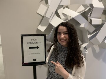 Alexandra Gonzalez points at a sign reading PR AI Community