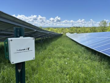 An acoustic monitor bearing the Cornell Lab of Ornithology K. Lisa Yang Center for Conservation Bioacoustics logo with solar panels in the background