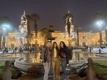 Holly Sexton with two colleagues in front of a fountain in a lit plaza at night