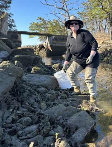 Harmony Borchard-Wier holds a bucket while standing on the bank of a creek