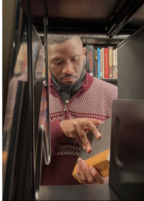 Amir Douglas seen through a library shelf holding a book