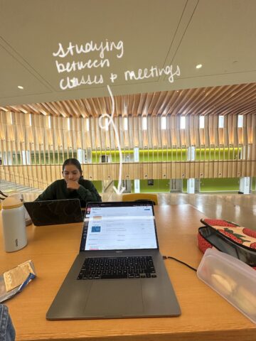 A laptop is open on a table with another person sitting on the other side