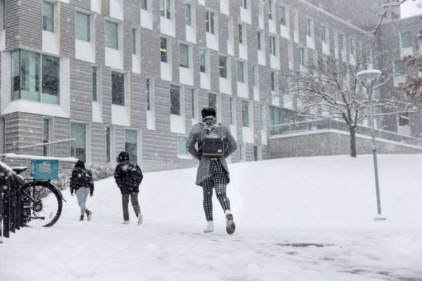 Students walk on a snow-covered path on Cornell's campus while snow continues to fall around them