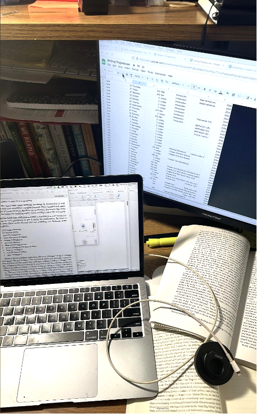 A laptop, computer monitor, open book, and open notebook on a table