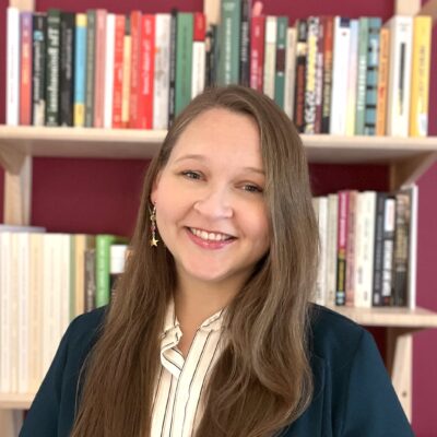 Dusti Bridges smiles in front of a full bookshelf