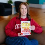 Vicki Johnson wears a Cornell sweatshirt and holds up a copy of her book, Pitch Your Potential: The Formula to Win Selective Opportunities and Leverage Your Story for Success.