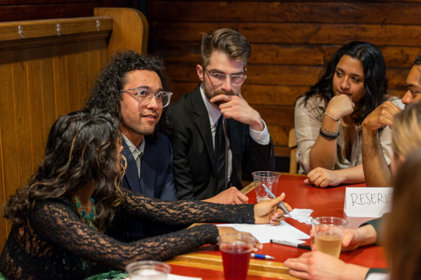Students participate in a trivia event at the Big Red Barn, with several students in thought while another prepares to write down their answer