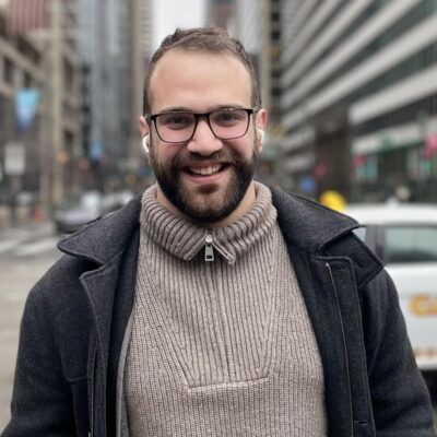 Filippos Tzortzoglou stands on a city street with tall buildings and vehicles in the background