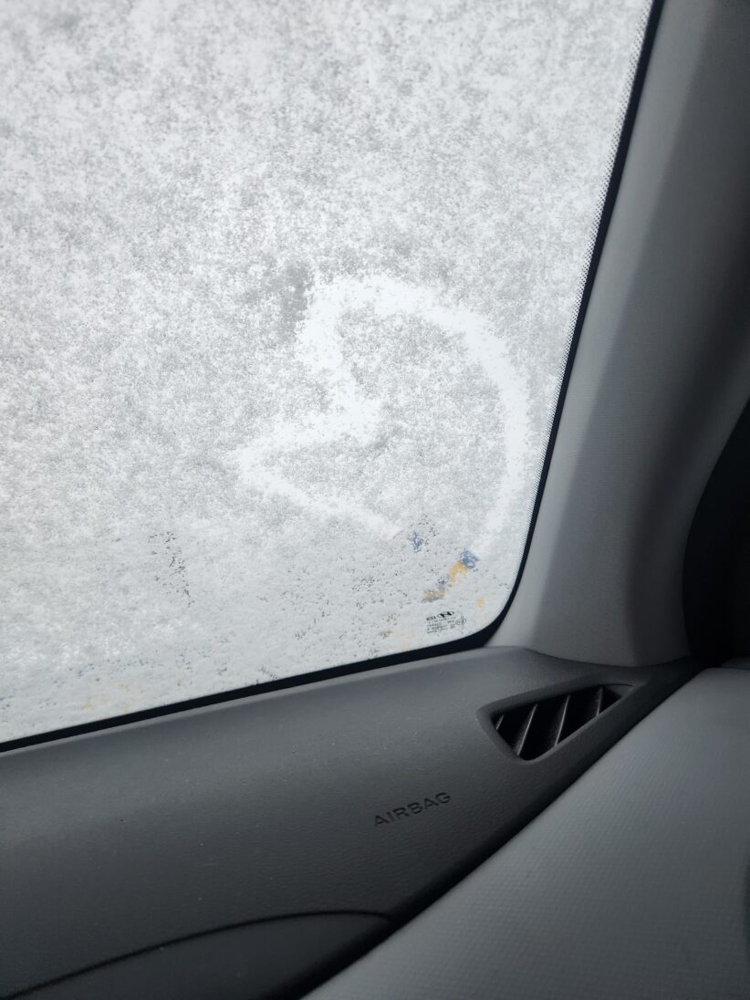 A heart drawn in the snow on a car windshield as seen from inside the car