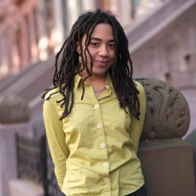 Nia Whitmal stands on a city sidewalk with brownstone buildings behind her