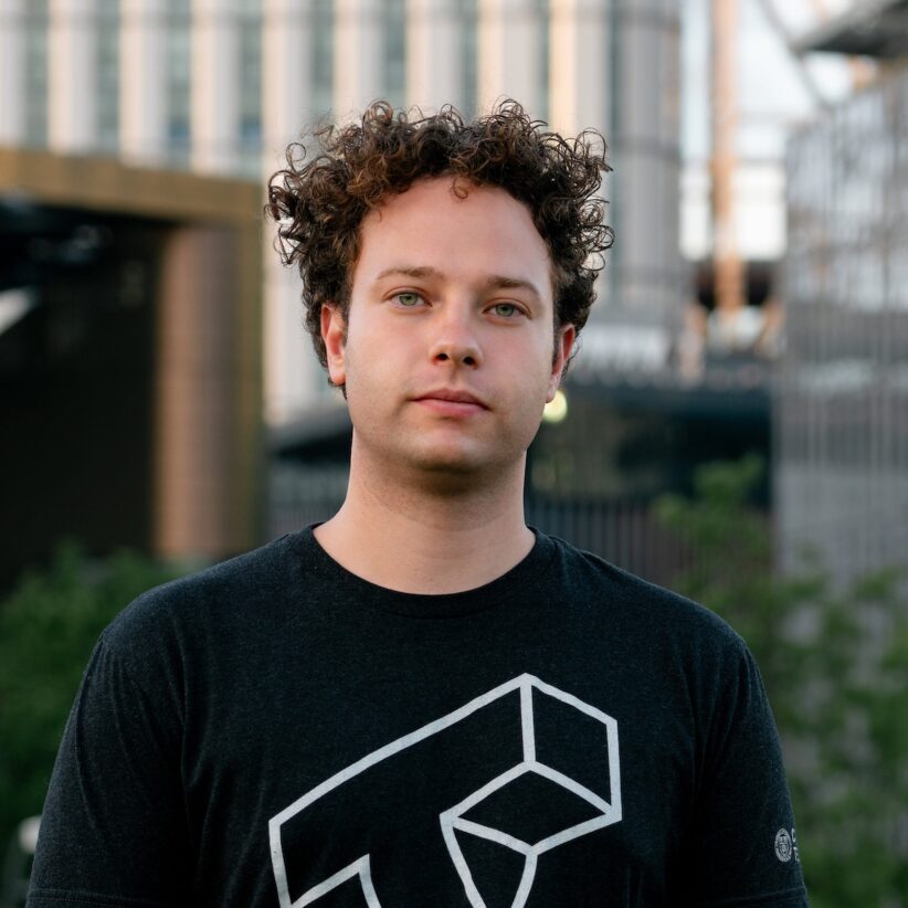 Jonathan Segal wears a Cornell Tech shirt and stands outside with buildings in the background