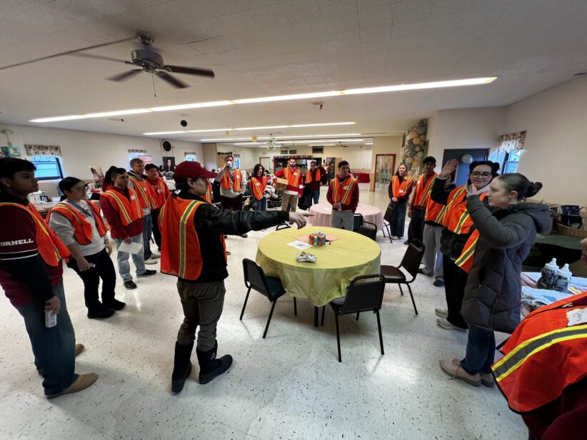 A group of volunteers in bright safety vests stands in a circle while one volunteer gives instructions