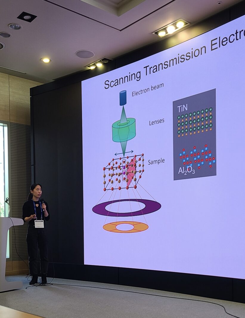 Clara Chung speaks into a microphone while standing next to a projected presentation