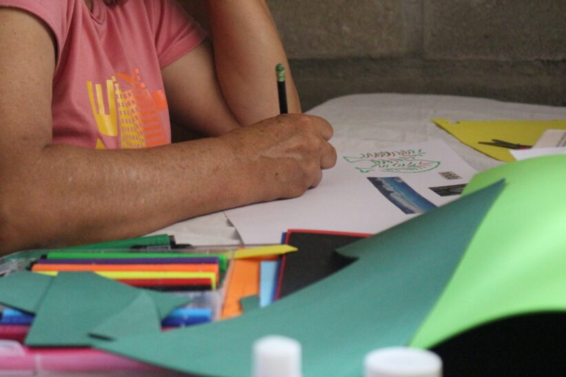 A person holds a pencil and draws on a piece of paper on the table in front of them